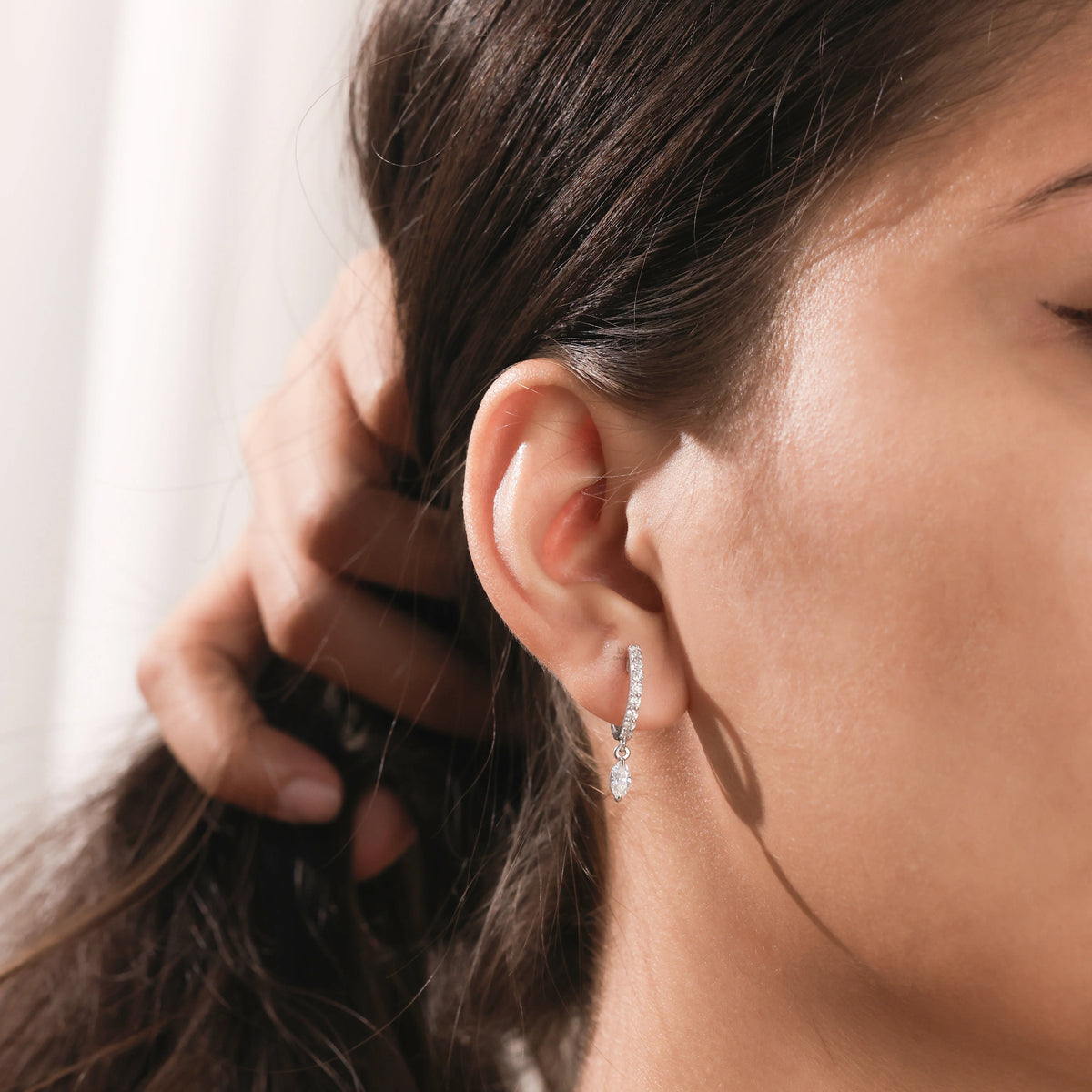 Elegantly styled ear with a round and marquise diamond dangling hoop earring in white gold. Secured with a detailed prong setting.