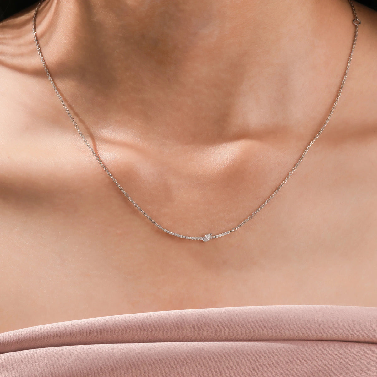 Woman wearing a delicate Round and Marquise diamond necklace featuring a prong and pave-set curved bar in 14K white gold.