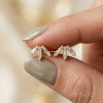 Close-up shot of a hand holding a pair of prong-set baguette and round diamond stud earring studs in yellow gold, showcasing a geometric arch design.