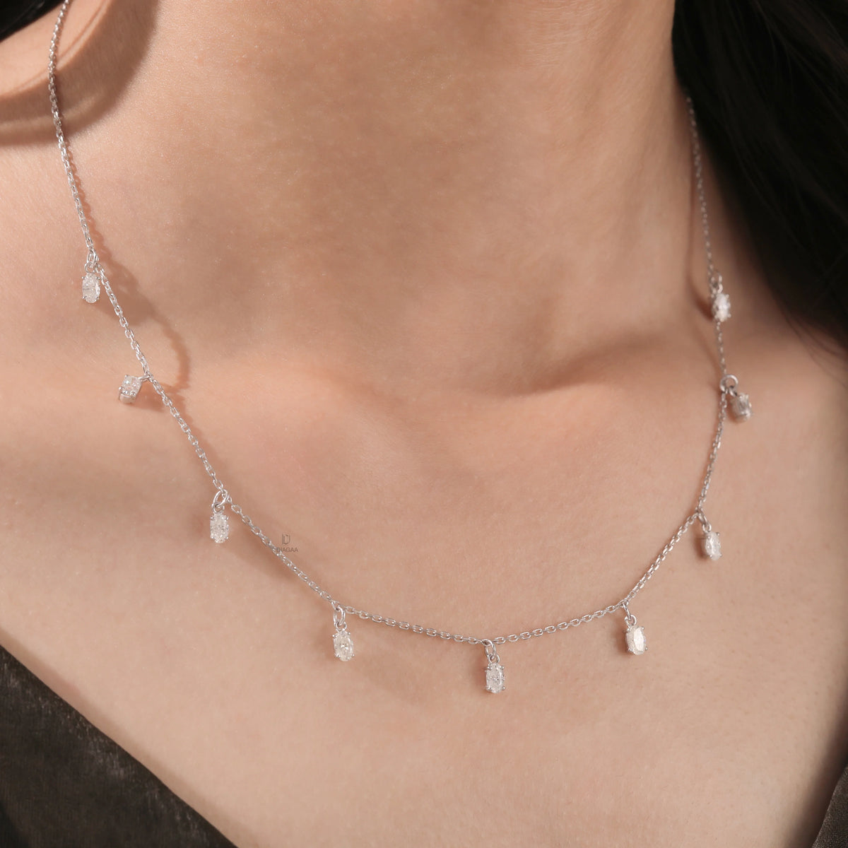 Model wearing a nine-stone prong-set Oval diamond dangling necklace in yellow gold, shown resting on the collarbone above a dark top.