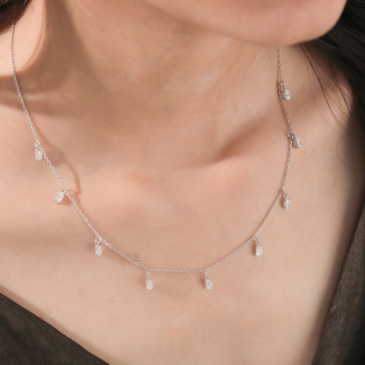 Model wearing a nine-stone prong-set Oval diamond dangling necklace in yellow gold, shown resting on the collarbone above a dark top.