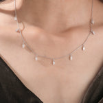 Model wearing a nine-stone prong-set Oval diamond dangling necklace in yellow gold, shown resting on the collarbone above a dark top.