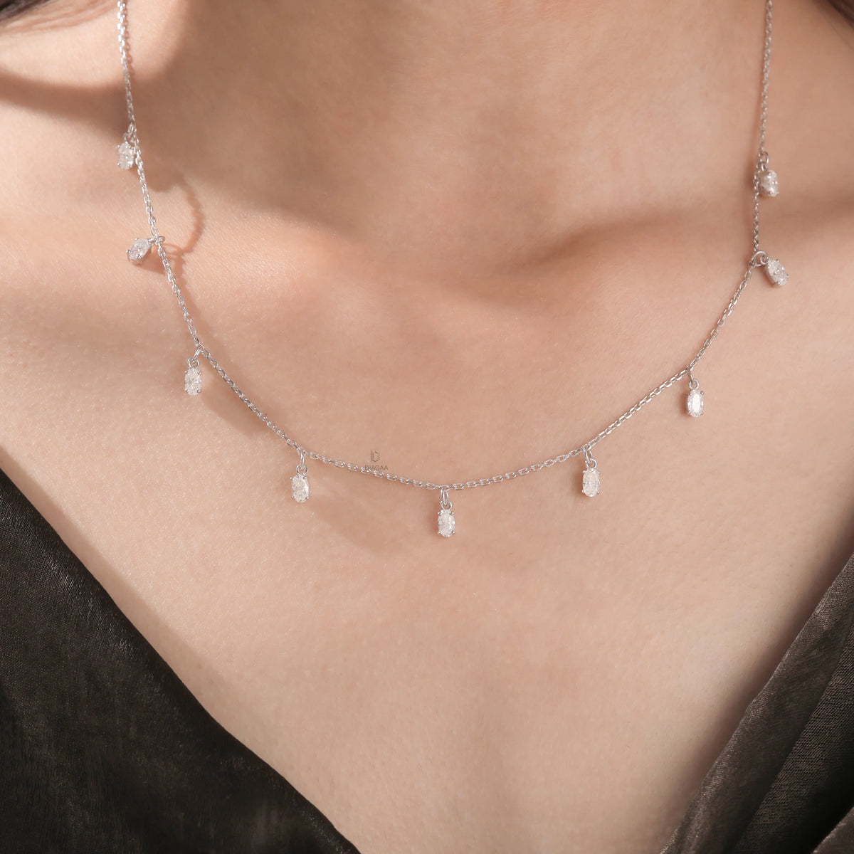 Model wearing a nine-stone prong-set Oval diamond dangling necklace in yellow gold, shown resting on the collarbone above a dark top.