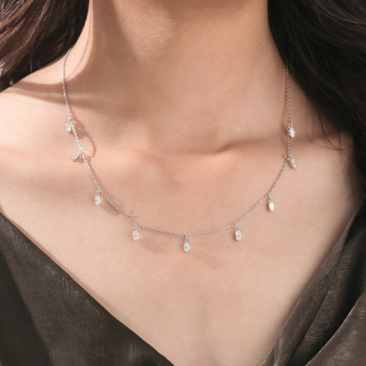 Model wearing a nine-stone prong-set Oval diamond dangling necklace in yellow gold, shown resting on the collarbone above a dark top.