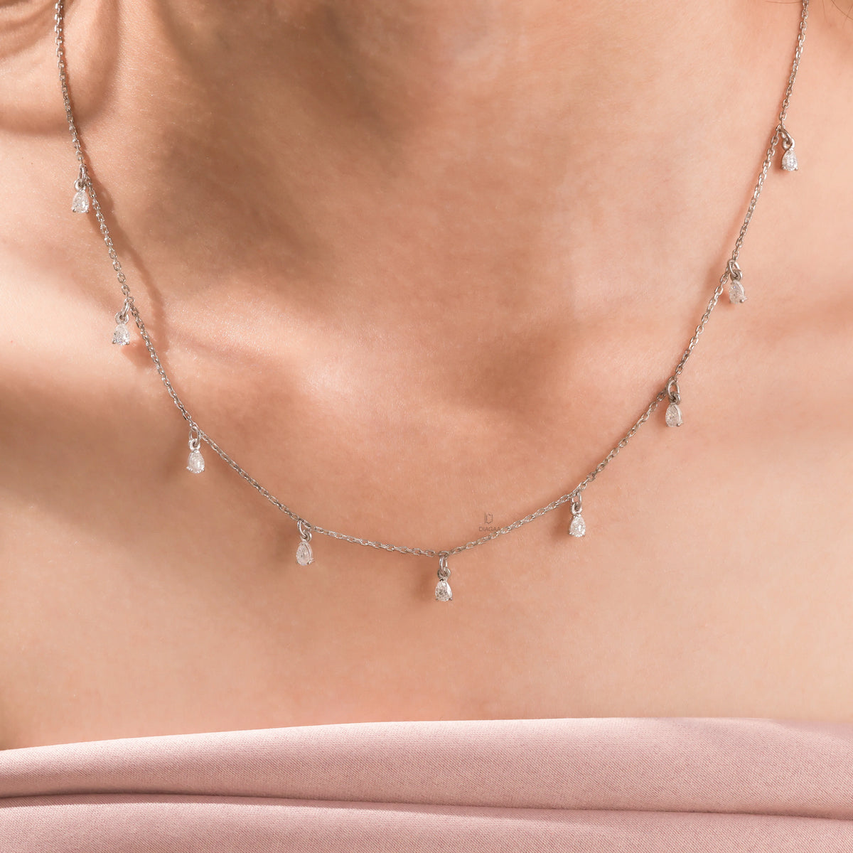 Elegant women's jewelry resting on a model's collarbone, featuring a nine-stone prong-set pear diamond dangling necklace crafted in yellow gold