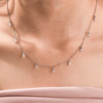 Elegant women's jewelry resting on a model's collarbone, featuring a nine-stone prong-set pear diamond dangling necklace crafted in yellow gold