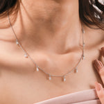 Elegant women's jewelry resting on a model's collarbone, featuring a nine-stone prong-set pear diamond dangling necklace crafted in yellow gold