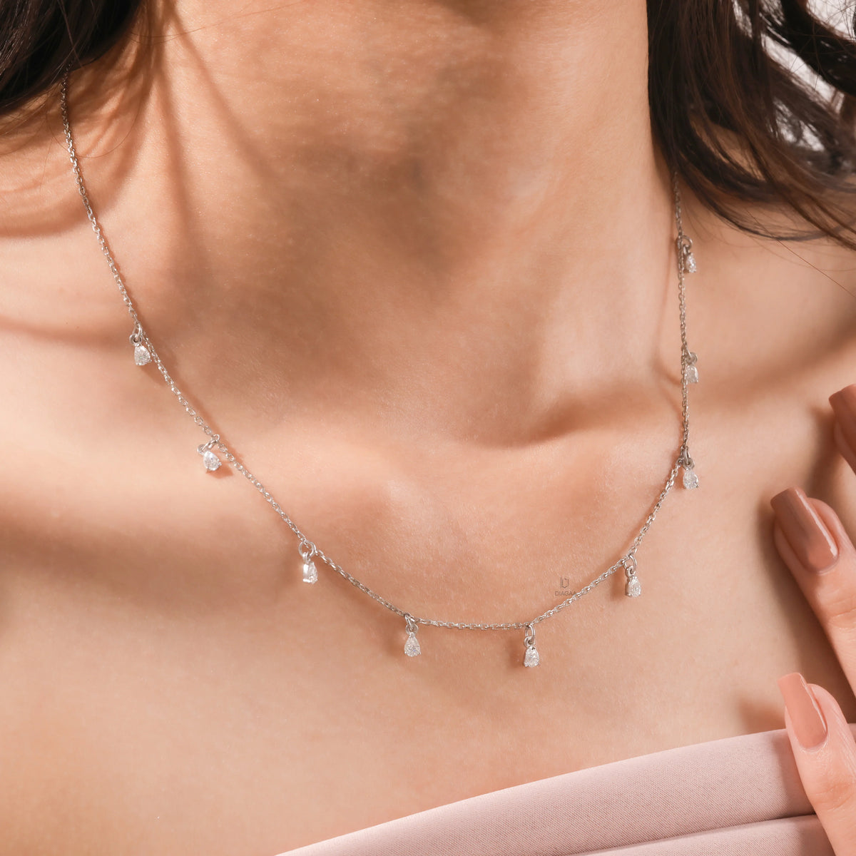 Elegant women's jewelry resting on a model's collarbone, featuring a nine-stone prong-set pear diamond dangling necklace crafted in yellow gold
