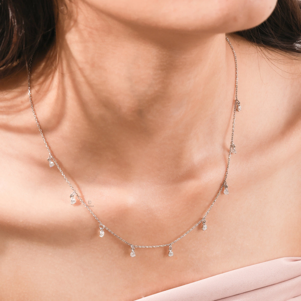 Elegant women's jewelry resting on a model's collarbone, featuring a nine-stone prong-set pear diamond dangling necklace crafted in yellow gold
