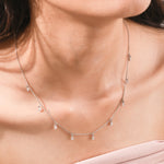 Elegant women's jewelry resting on a model's collarbone, featuring a nine-stone prong-set pear diamond dangling necklace crafted in yellow gold