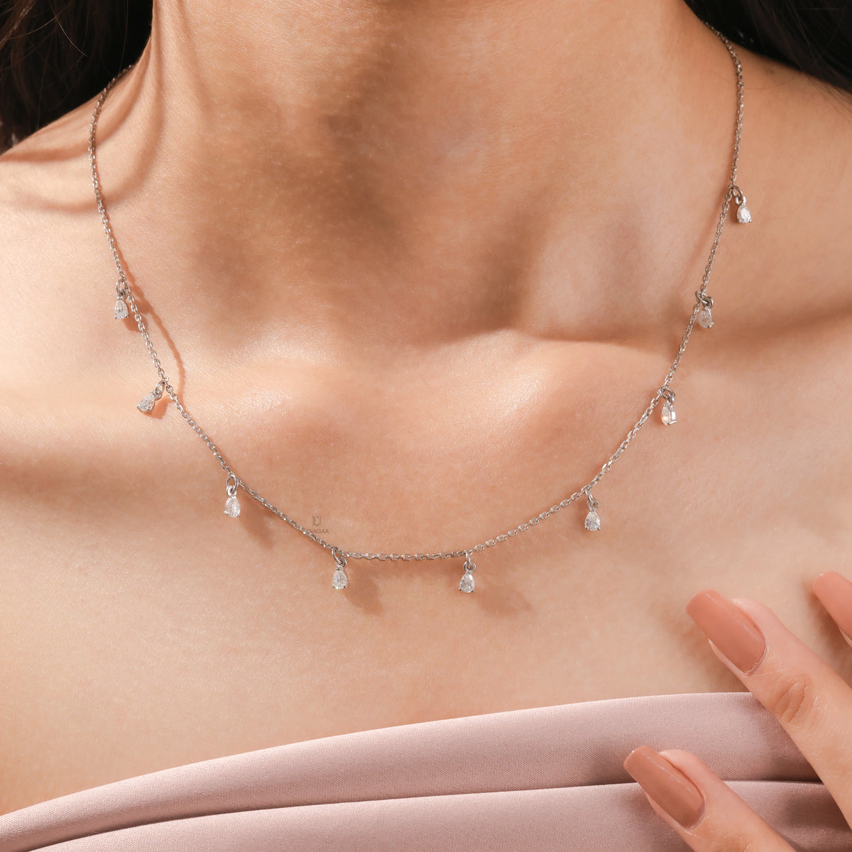 Elegant women's jewelry resting on a model's collarbone, featuring a nine-stone prong-set pear diamond dangling necklace crafted in yellow gold