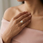 Oval cut diamond engagement ring with a yellow gold milgrain bezel setting worn on a hand.