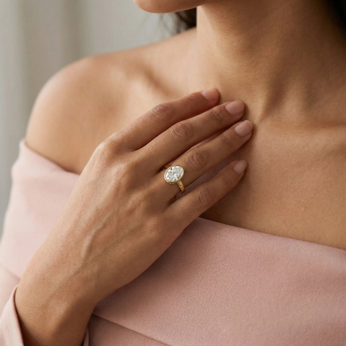 Oval cut diamond engagement ring with a yellow gold milgrain bezel setting worn on a hand.