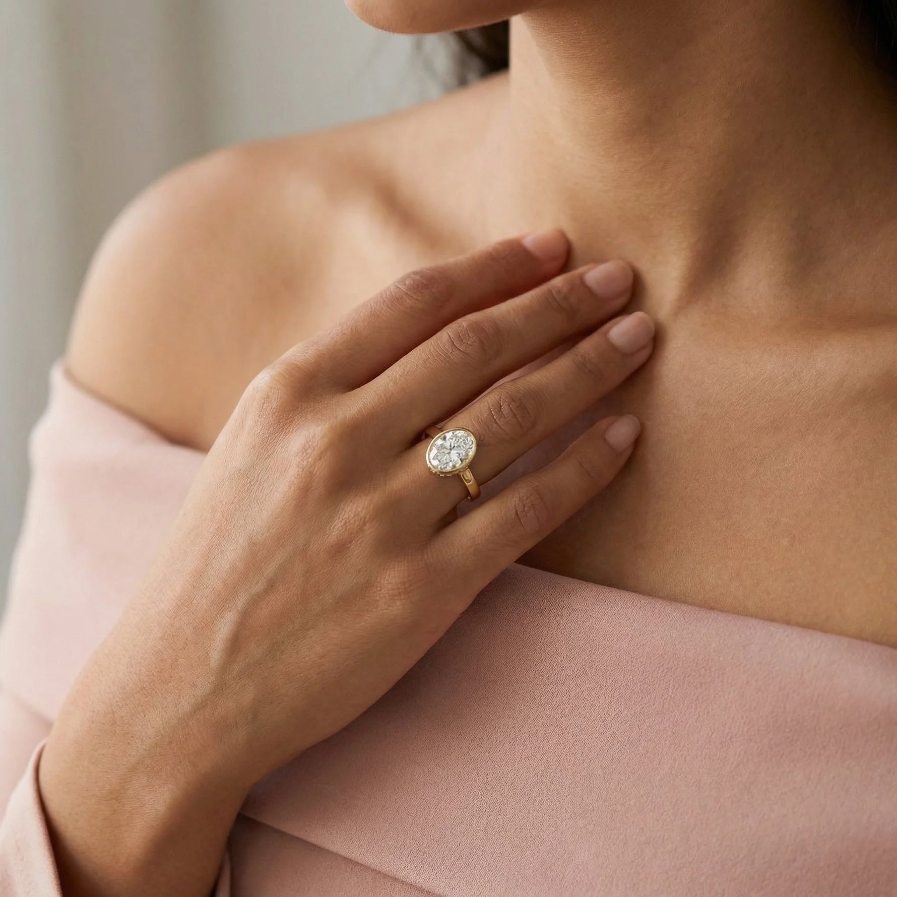 Oval cut diamond engagement ring with a yellow gold milgrain bezel setting worn on a hand.