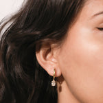 Model showcasing everyday fine jewelry: a small yellow gold hoop earring with an elegant oval-shaped clear diamond dangle earring.