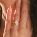 Hand modeled view of a yellow gold ring showcasing a Solitaire oval diamond ring. An elegant oval diamond ring crafted as a round diamond halo set ring gold ring style.