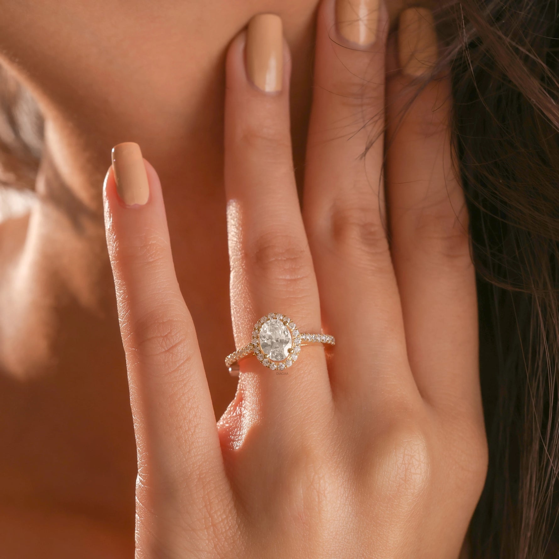 Close-up of an elegant hand wearing an oval halo engagement ring with a pavé band in yellow gold ring.