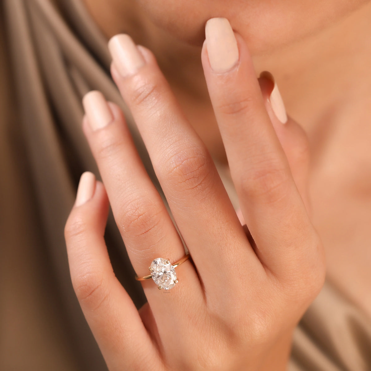 Close-up side profile of a yellow gold solitaire diamond engagement ring featuring an oval diamond and a delicate hidden halo setting worn on a finger.