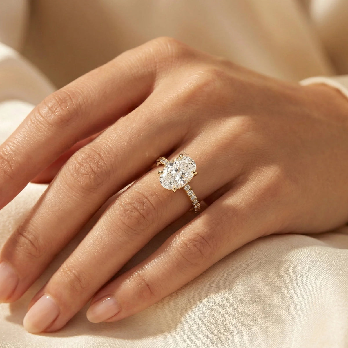 Oval cut diamond engagement ring featuring a large brilliant center stone and a yellow gold round cut siad stone pavé diamond band on a finger.