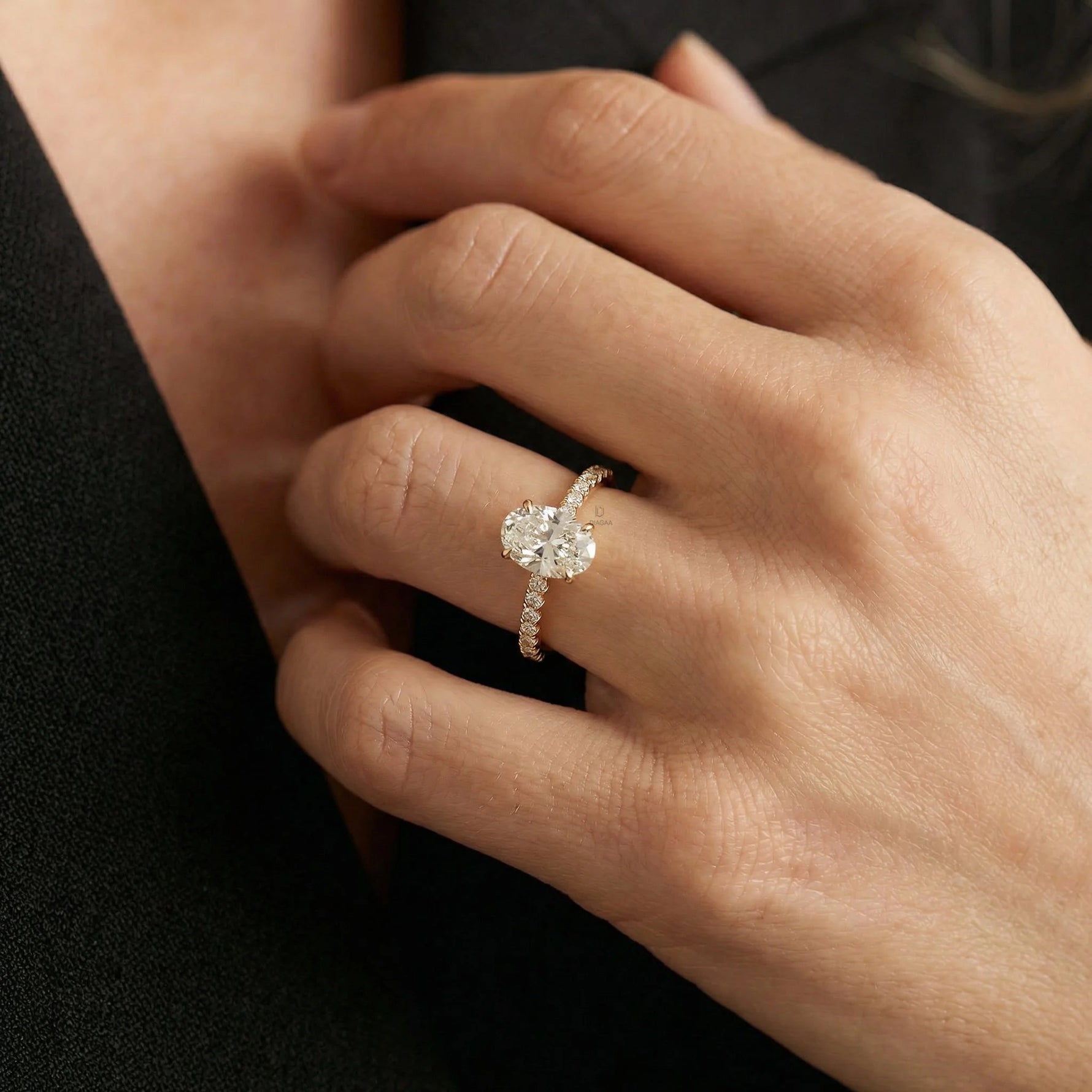Elegant yellow gold engagement ring featuring an oval center diamond and a delicate pave setting in a hand finger.