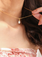 Woman wearing a delicate yellow gold oval diamond necklace featuring a prong-set solitaire pendant.