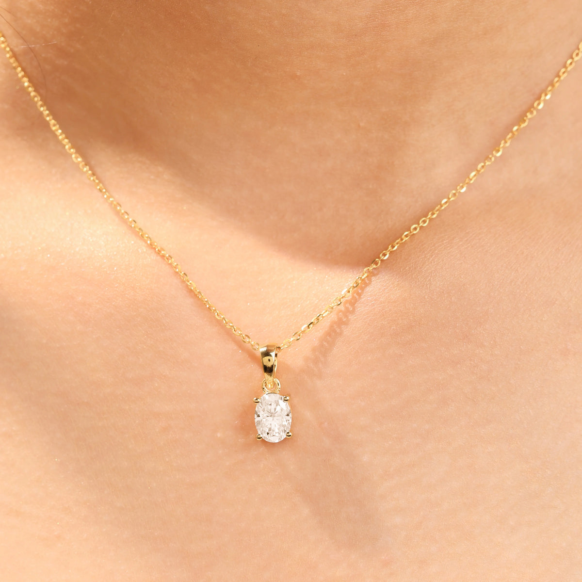 Woman wearing a delicate yellow gold oval diamond necklace featuring a prong-set solitaire pendant.