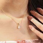 Woman wearing a delicate yellow gold oval diamond necklace featuring a prong-set solitaire pendant.