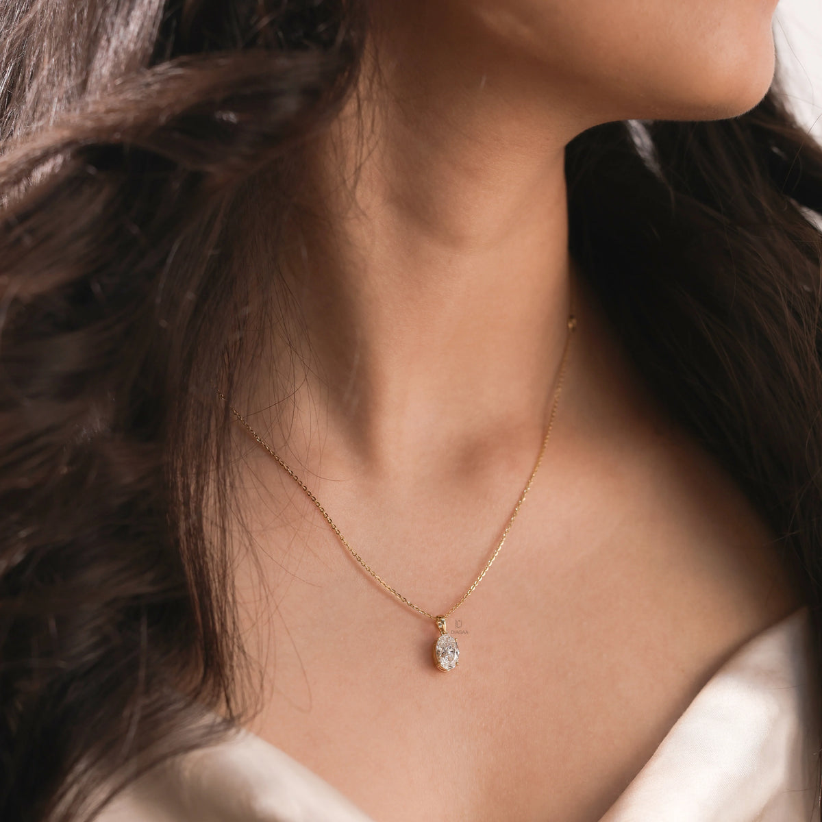 Woman wearing a delicate 18K yellow gold oval diamond necklace featuring a sparkling prong-set solitaire pendant.