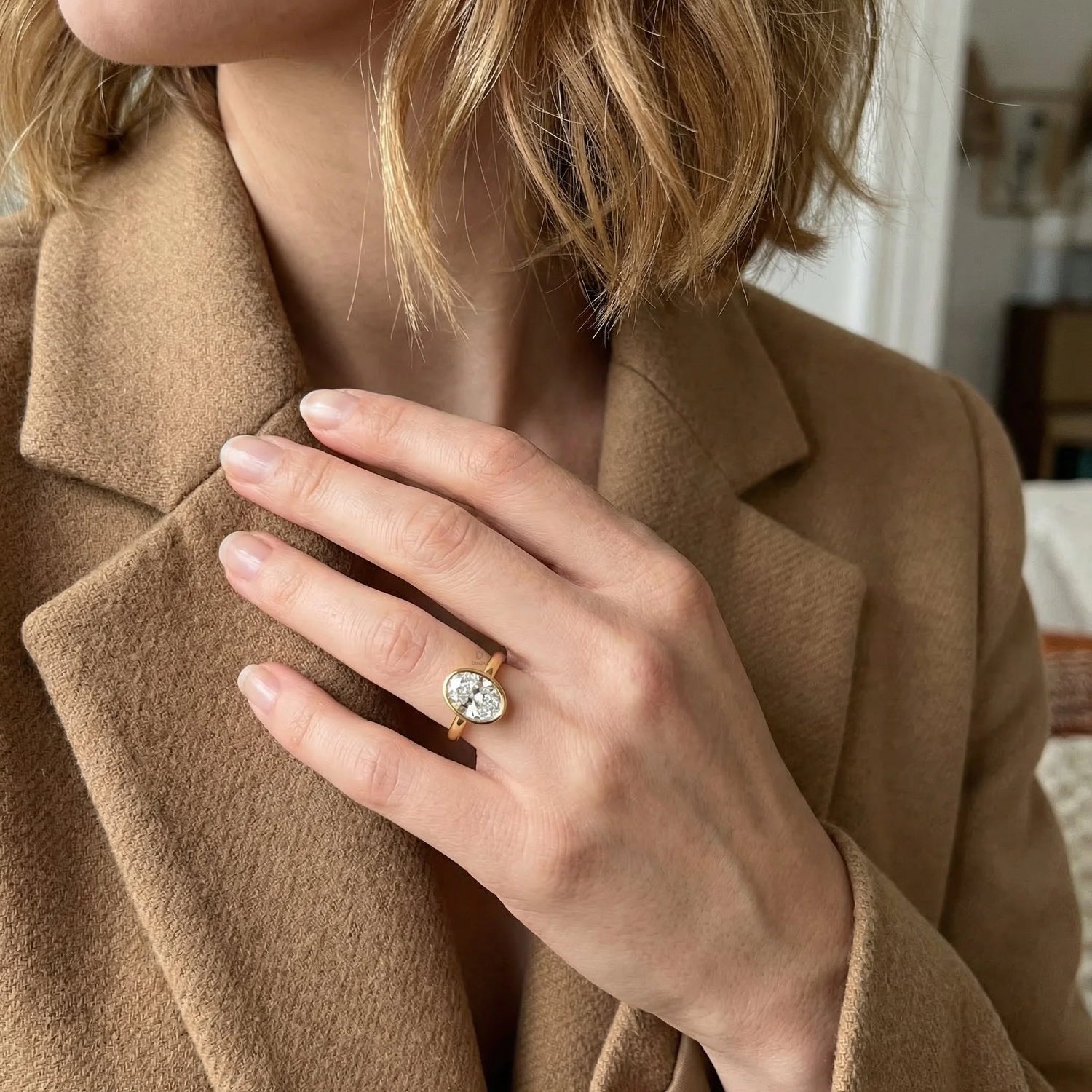 Minimalist yellow gold bezel solitaire ring featuring a brilliant oval diamond, displayed gracefully on a woman’s ring finger for a modern bridal look.