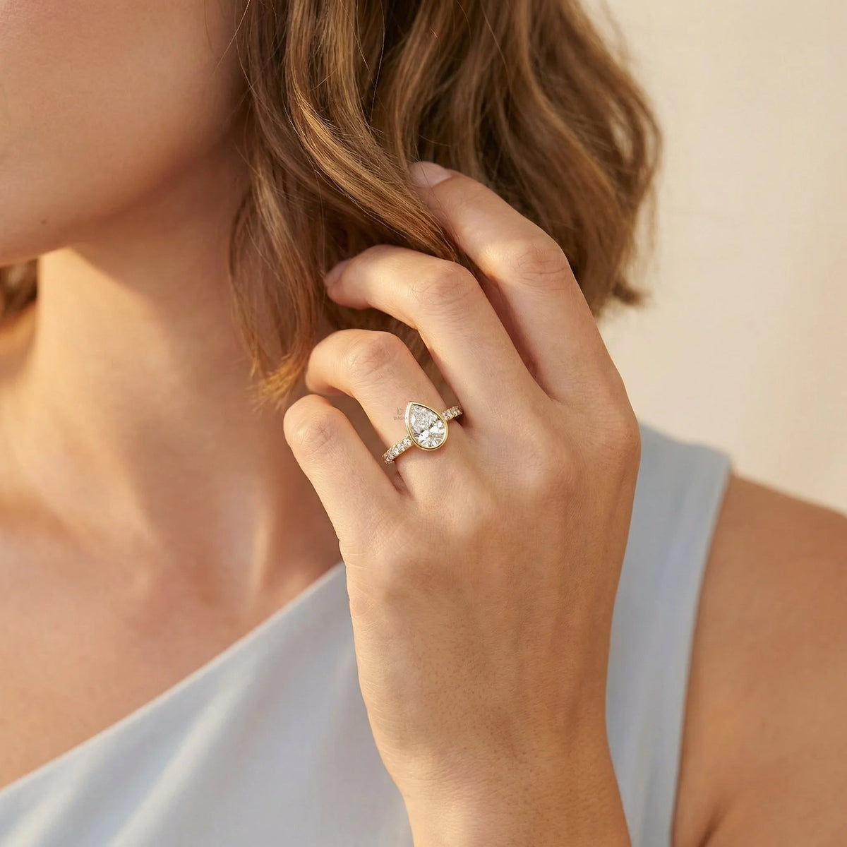 Close-up of a woman wearing a gold pear-cut diamond engagement ring with a round cut pavé set side band and bezel setting.