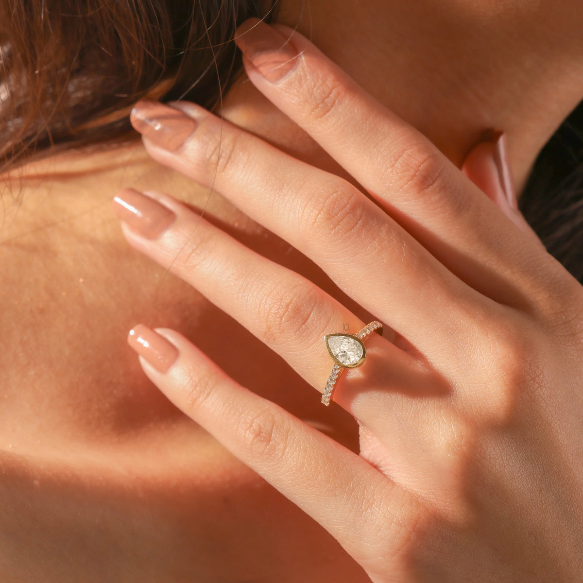 Pear cut diamond engagement ring with a yellow gold bezel setting and pavé band, worn on a hand to show everyday scale and styling.