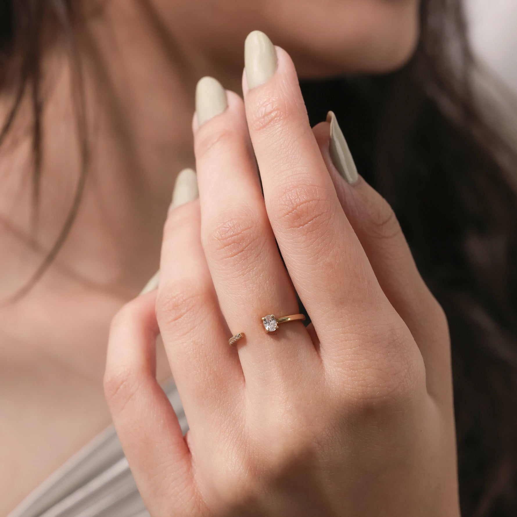 Dainty modern gold wrap ring featuring a single oval diamond and round  accent diamond paired with light sage green nails.