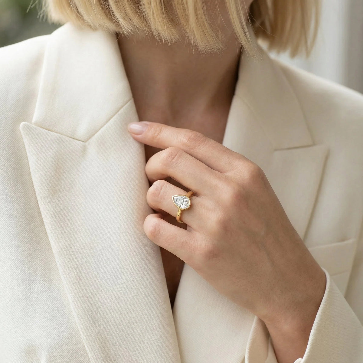 Minimalist yellow gold bezel solitaire engagement ring featuring a teardrop pear diamond, displayed gracefully on a woman’s ring finger for a modern bridal look.