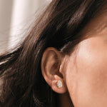 Woman wearing a gold bezel teardrop diamond stud earring. Dainty pear-shaped gemstone stud for ear lobe piercing, elegant fine jewelry
