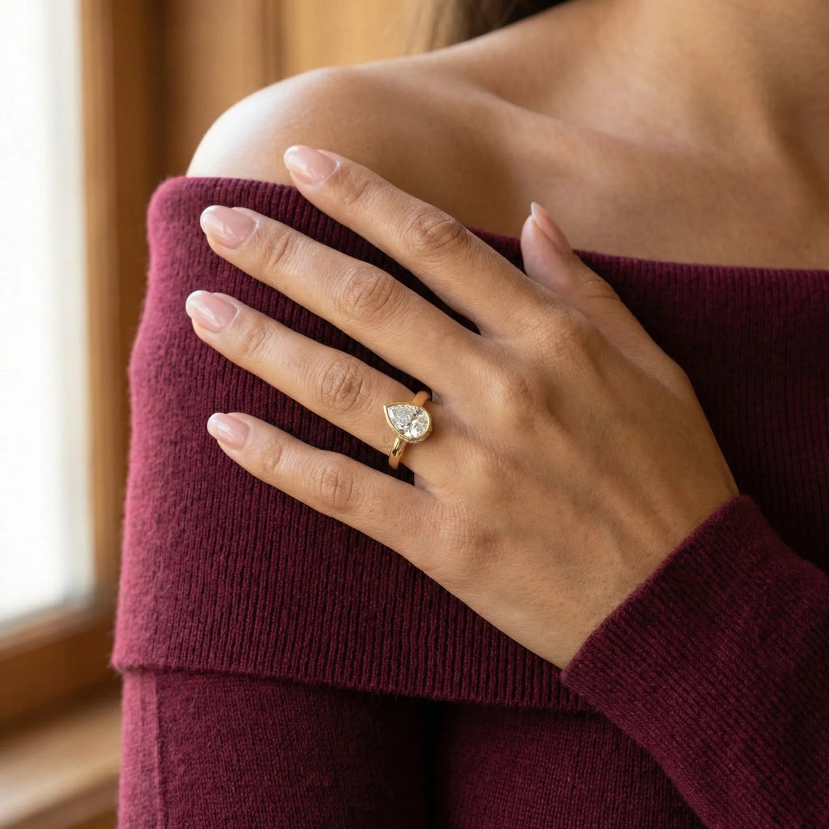 Pear cut diamond engagement ring with a yellow gold bezel setting worn on a model's hand.