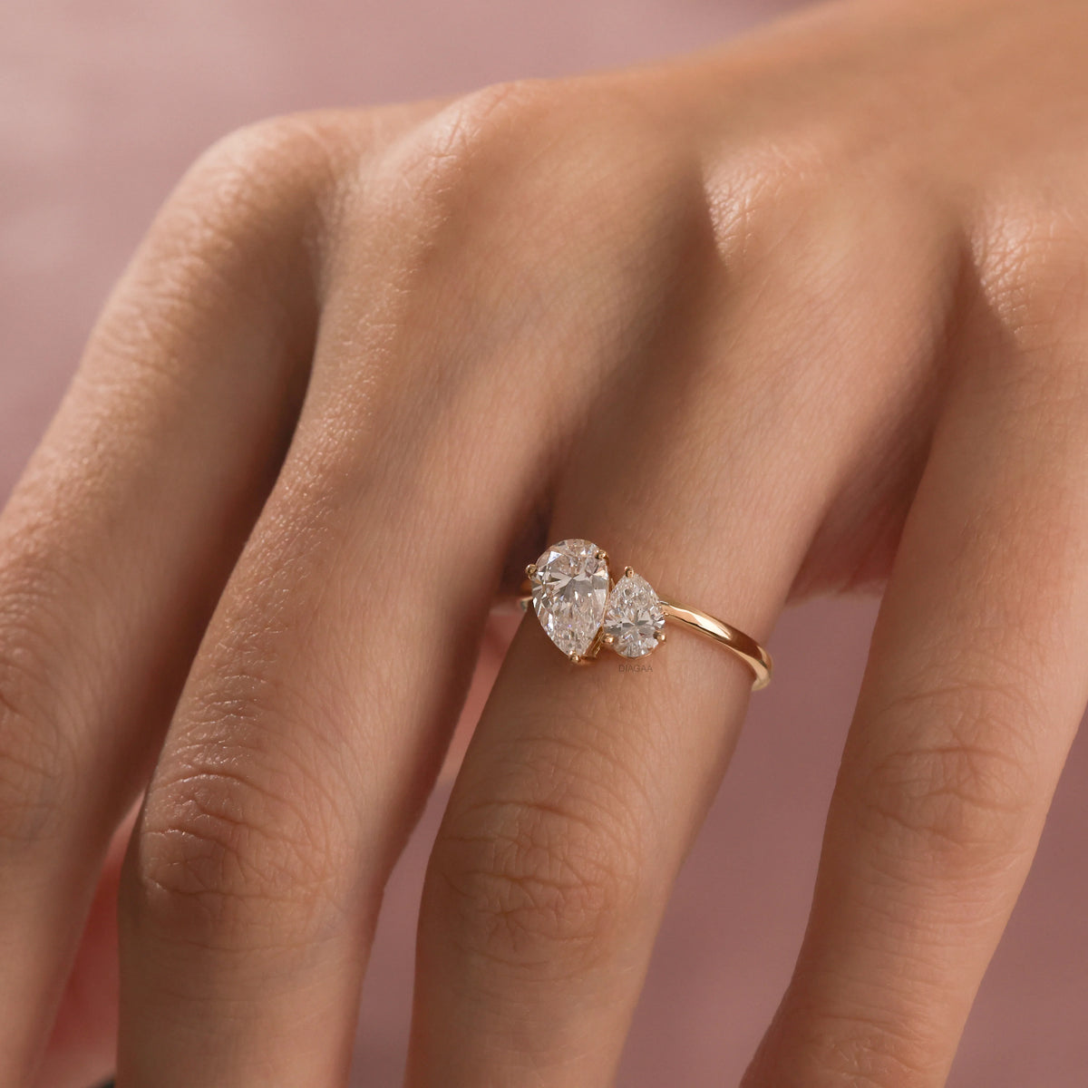 A close-up of a hand wearing a delicate yellow gold Toi et Moi ring. The ring features two prong-set, pear-cut diamonds side-by-side engagement ring 