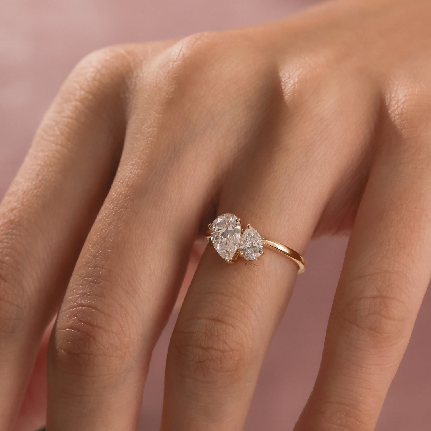 A close-up of a hand wearing a delicate yellow gold Toi et Moi ring. The ring features two prong-set, pear-cut diamonds side-by-side engagement ring 