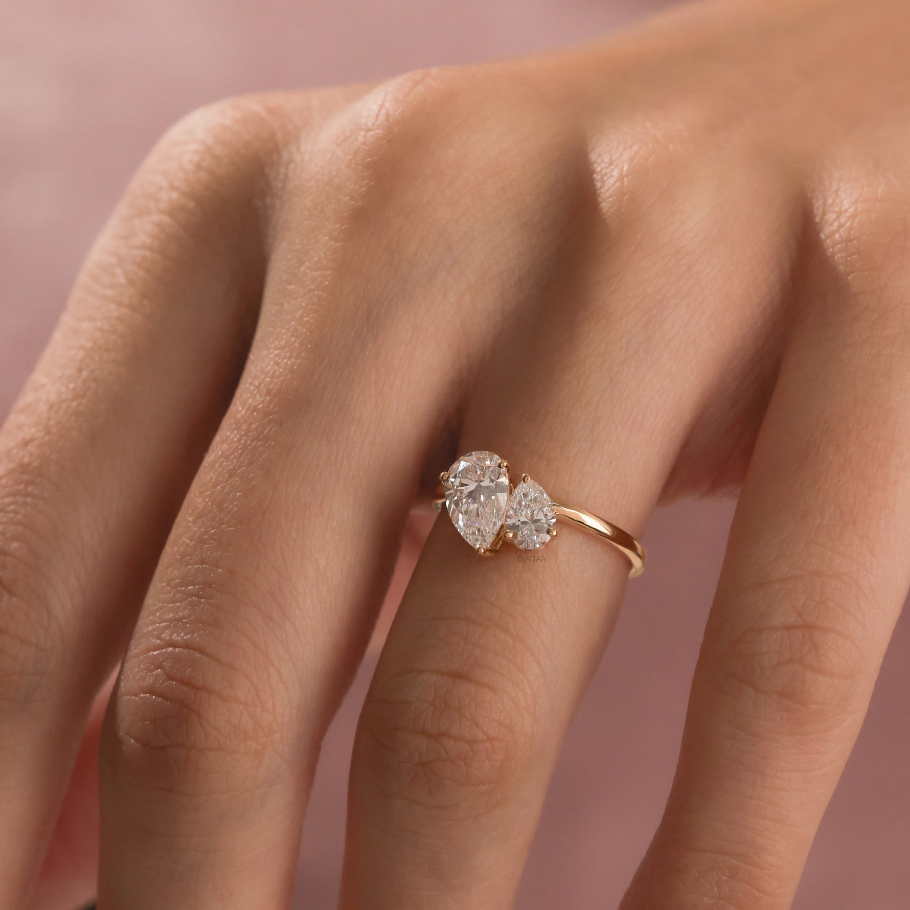 A close-up of a hand wearing a delicate yellow gold Toi et Moi ring. The ring features two prong-set, pear-cut diamonds side-by-side engagement ring 