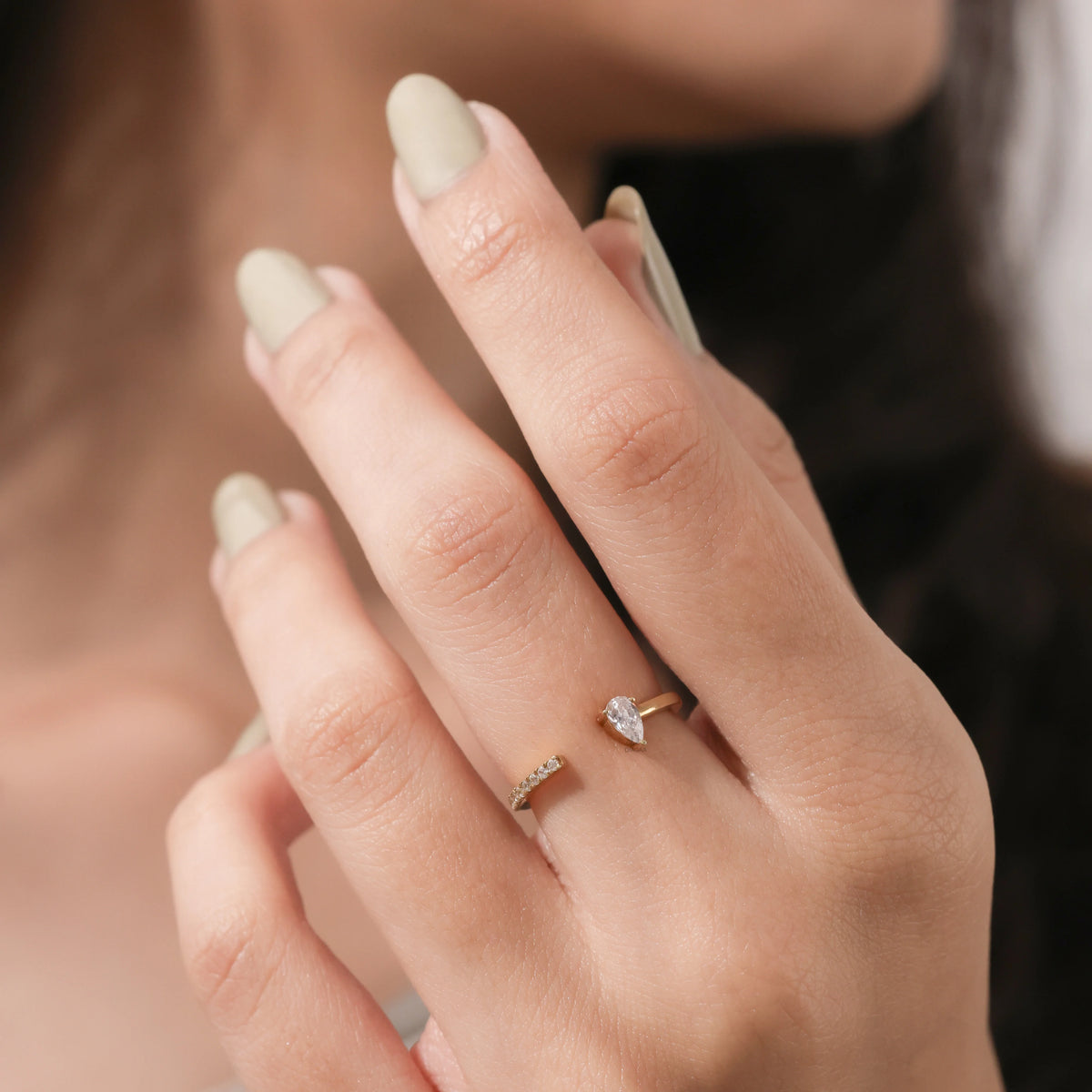 Gold open cuff ring featuring a pear-cut diamond and a pave diamond band on a woman's hand.