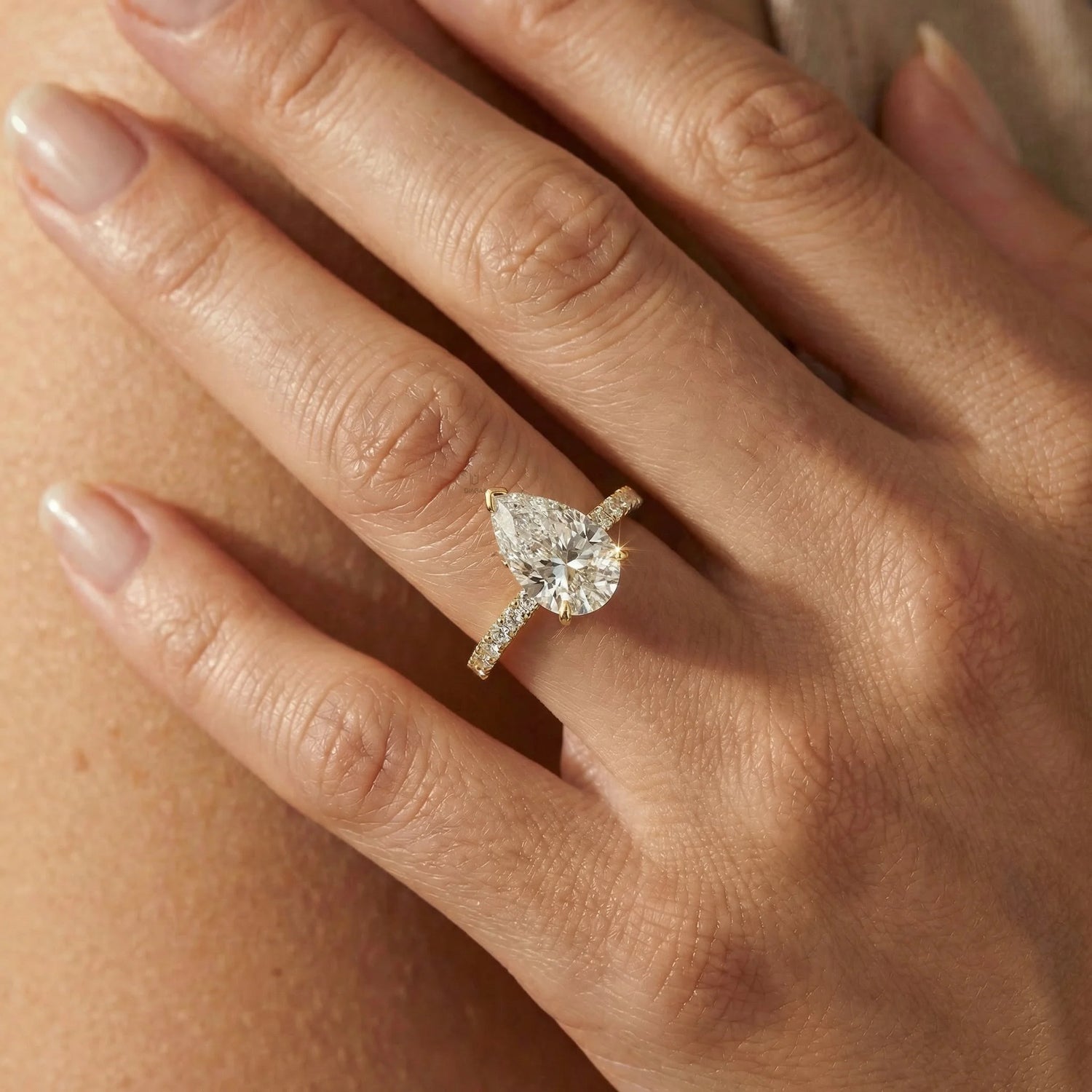 Elegant pear cut solitaire ring with a delicate yellow gold diamond accent band, ideal for a modern wedding ring look.