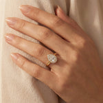 Hand wearing a 14k yellow gold pear diamond ring against . This unique Solitaire pear diamond ring showcases a bright center stone band. round diamond halo set ring.