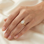 Hand wearing a yellow gold pear diamond ring against . This unique Solitaire pear diamond ring showcases a bright center stone band. round diamond halo set ring.