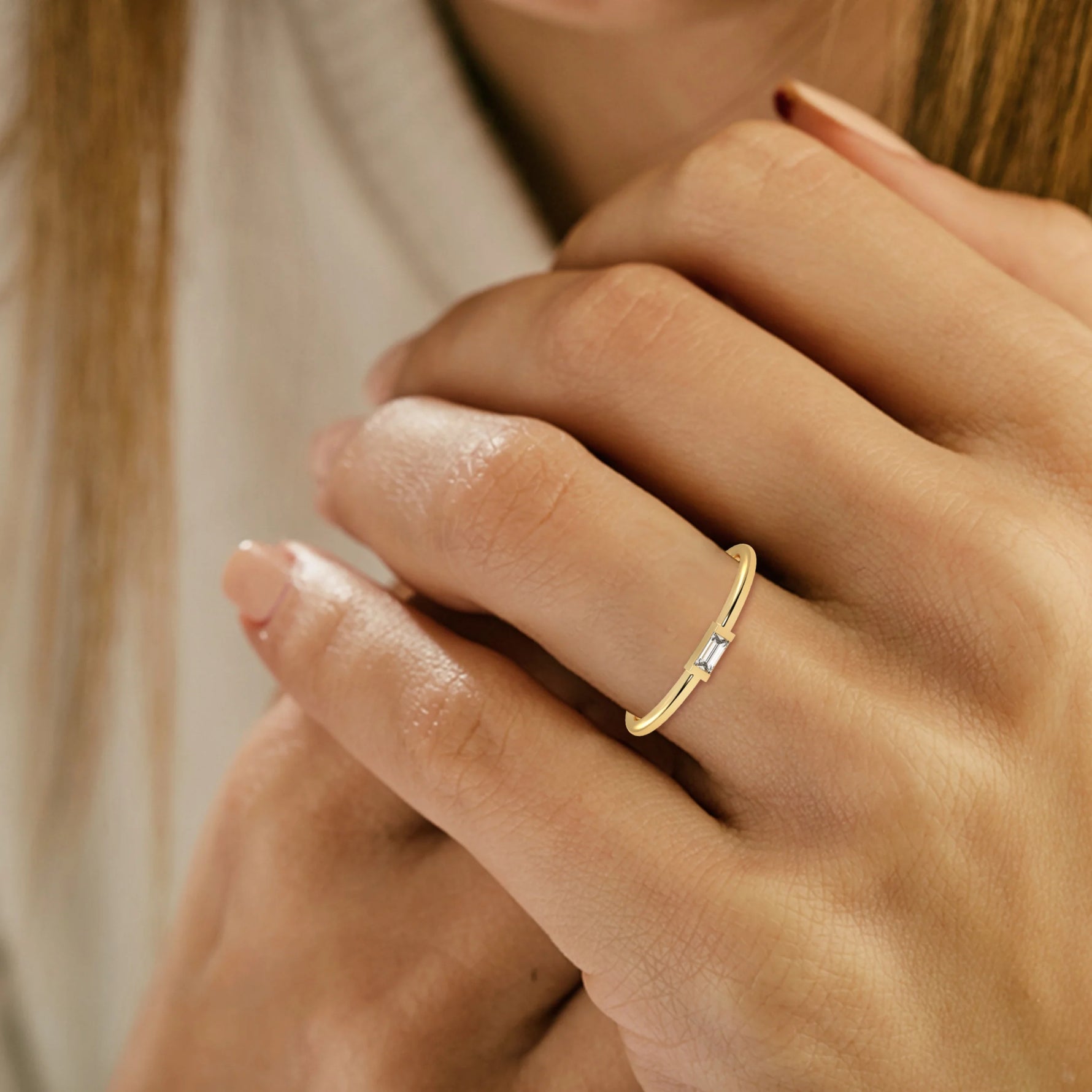 This yellow gold A thin gold band showcases a baguette diamond held in a bar prong setting on ring finger