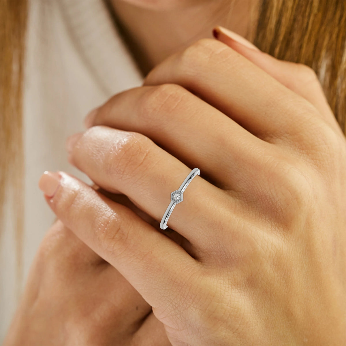 Thin white gold band with a round solitaire diamond in a hexagonal bezel setting on ring finger