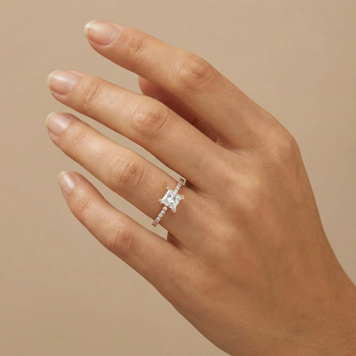 Princess cut diamond engagement ring in gold worn on a hand, featuring a brilliant square center stone and a slender shimmering pave diamond band.
