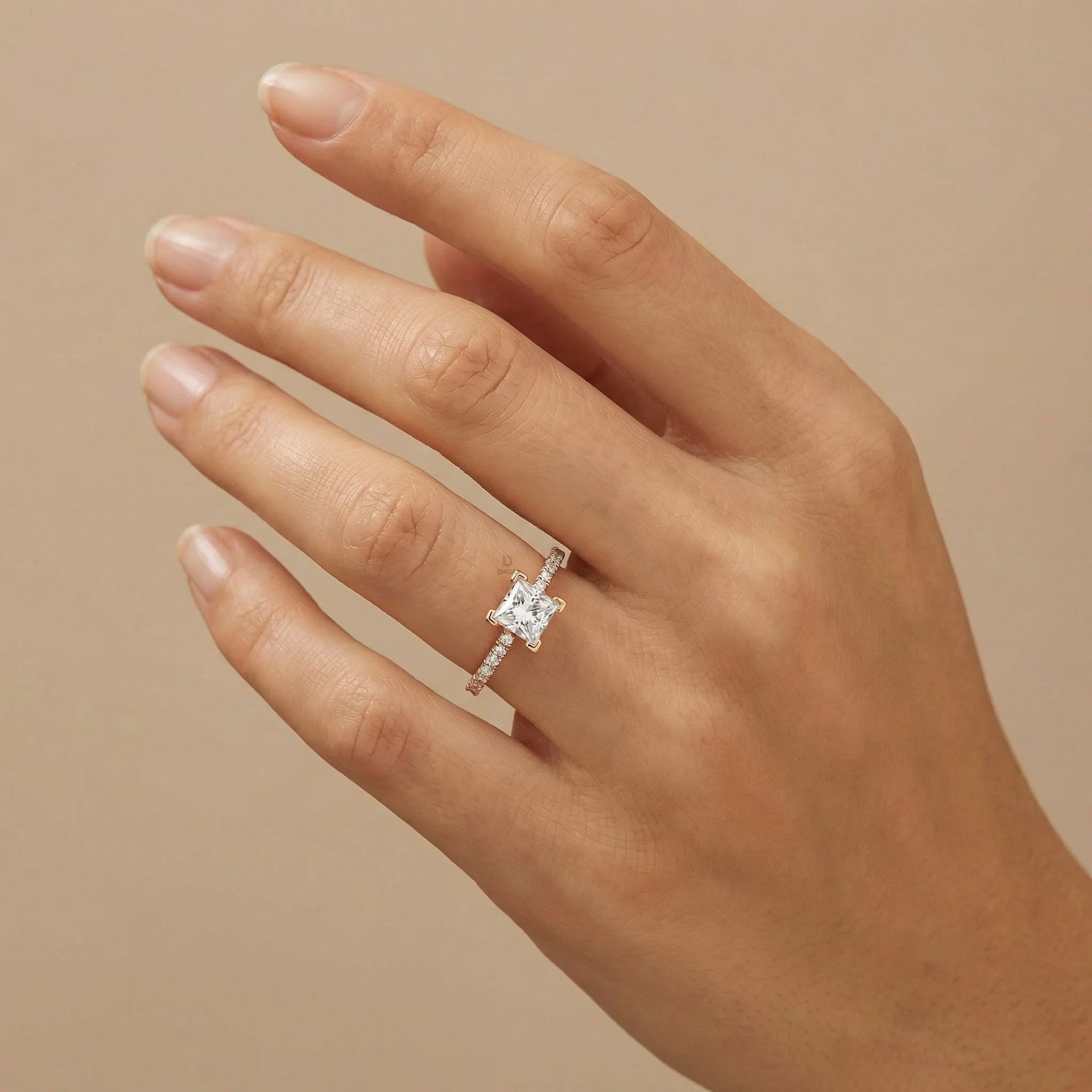 Princess cut diamond engagement ring in gold worn on a hand, featuring a brilliant square center stone and a slender shimmering pave diamond band.