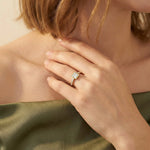 Close-up of a 10k yellow gold princess-cut diamond engagement ring with a modern bezel setting and shimmering pavé band, styled on a woman's hand wearing an olive green top.