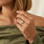 Close-up of a yellow gold princess-cut diamond engagement ring with a modern bezel setting and shimmering pavé band, styled on a woman's hand wearing an olive green top.