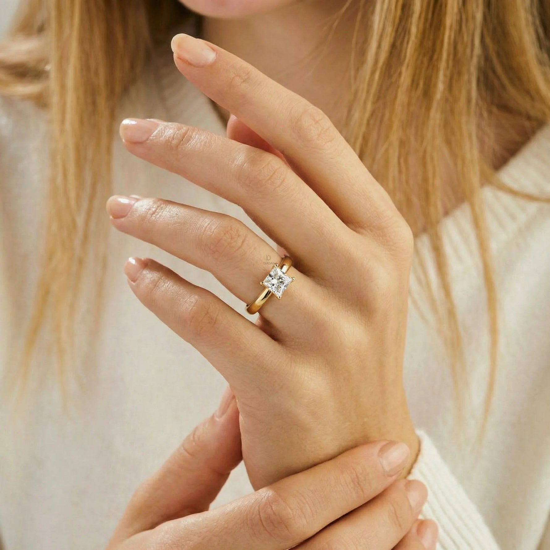 Close-up of a woman's hand wearing a classic 14k yellow gold solitaire engagement ring featuring a square princess cut diamond on her ring finger.