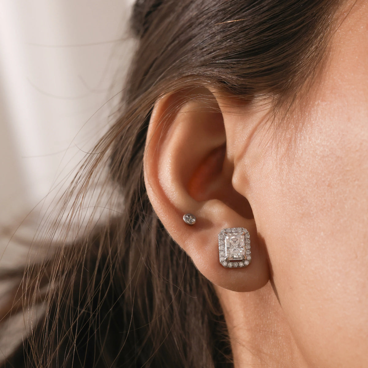  A close-up of radiant cut earrings featuring a sparkling diamond halo, paired with classic round diamond studs in 18K yellow gold.